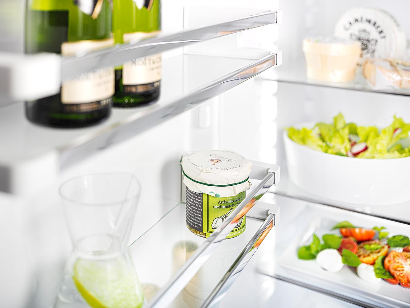 Foto eines Kühlschrankdetails mit Lebensmitteln. Glasborde Chrom-Reeling fotografiert mit Fachkamera und bewusster Schärfe-Verlagerung